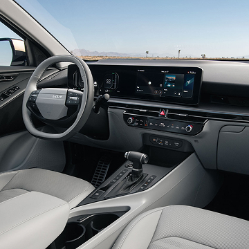 Interior view of the 2027 Kia Niro Hybrid SUV showcasing the steering wheel, grey front seats, center console, and dashboard. Desert landscape is visible through the windshield.