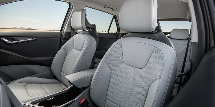 Interior view of the 2027 Kia Niro Hybrid Electric SUV focusing on the grey front driver and passenger seats, with a blue sky visible through the windows behind.