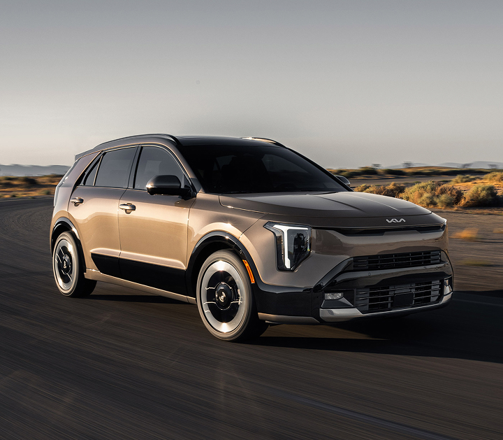 Front passenger side angle photograph of the 2027 Kia Niro Hybrid Electric SUV driving around a curved desert road in the sun.