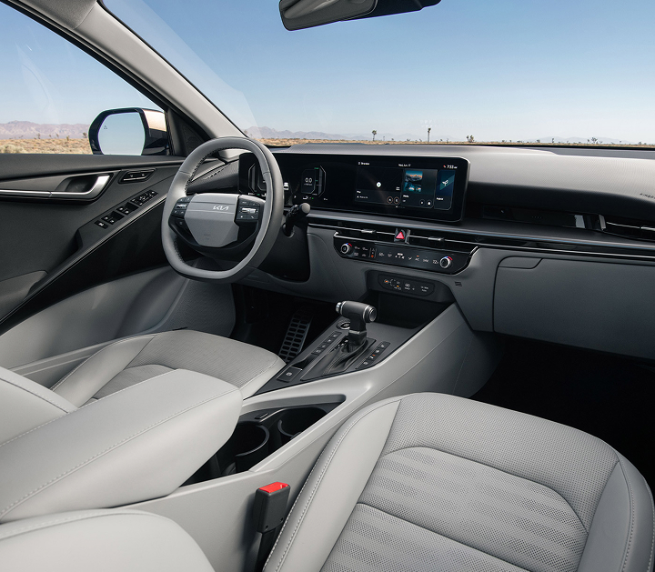 Interior view of the 2027 Kia Niro Hybrid SUV showcasing the steering wheel, grey front seats, center console, and dashboard. Desert landscape is visible through the windshield.