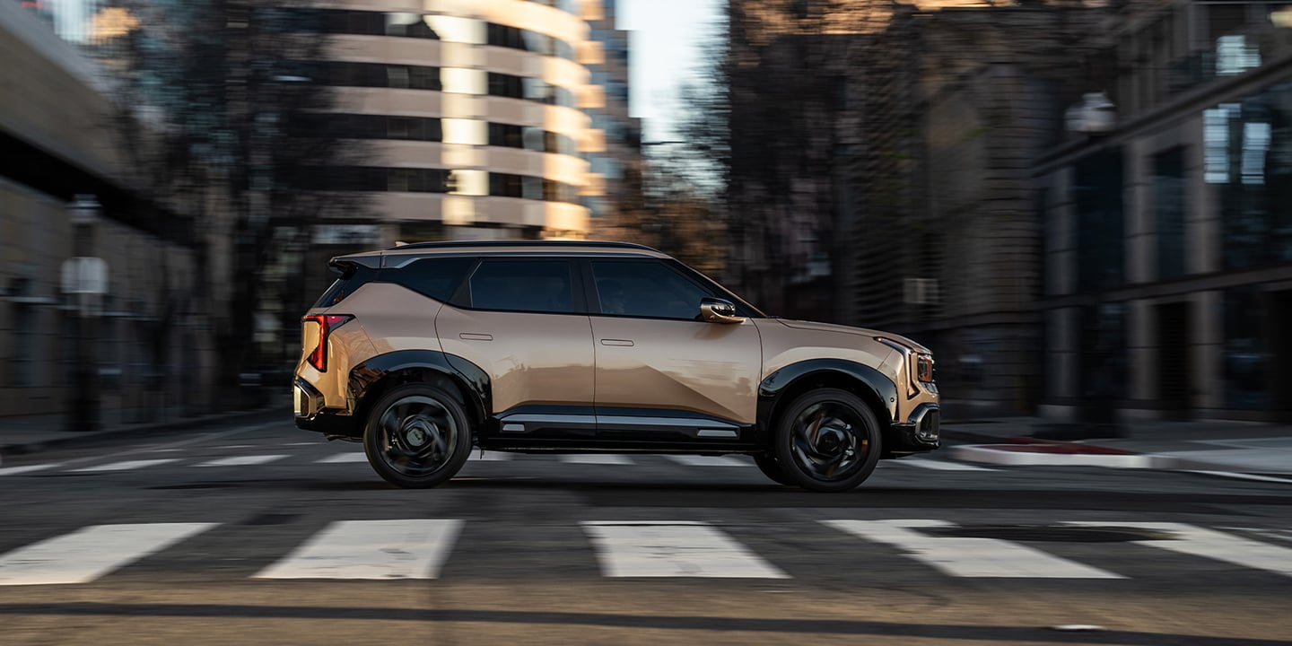 The 2027 Kia Seltos in brown driving through an urban setting, shown in full side profile with black wheels and chrome accent trims highlighting its modern exterior design.
