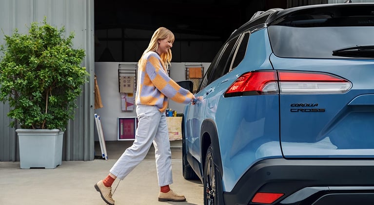 A woman going to open the driver's side door while talking on a smartphone